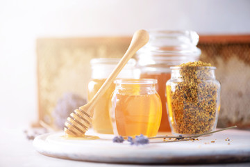 Bee pollen granules, honey jar with wooden dropper, honeycomb on grey backdrop. Copy space. Autumn harvest concept