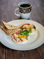 Hot breakfast on old wooden table. A pair of fried eggs with meat, vegetables and cheese on a white plate with a cup of hot coffee.