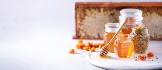 Herbal honey in jar with dipper, honeycomb, bee pollen granules, calendula flowers on grey background. - obrazy, fototapety, plakaty