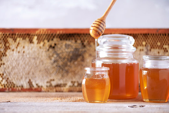 Honey dripping from wooden honey spoon in jar on grey background. Copy space. Autumn harvest concept. Banner