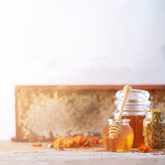 Herbal honey in jar with dipper, honeycomb, bee pollen granules, calendula flowers on grey background.