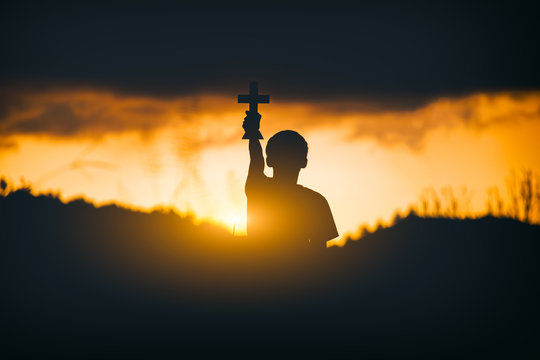 Young christian holding and lift the Cross at sunset background. christian silhouette concept.