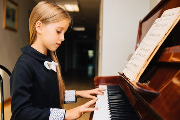 Little girl in a black dress learns to play the piano. The child plays a musical instrument.