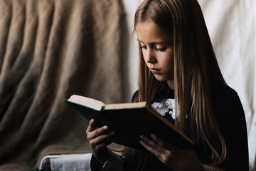 Little girl in a black dress holds a green book and reads it.