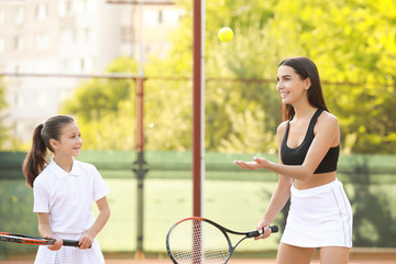 Little girl and her mother playing tennis on court