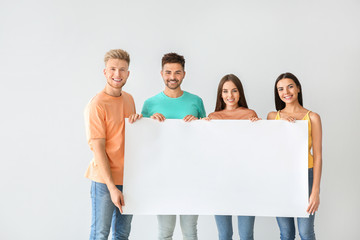 Group of young people in stylish casual clothes and with blank poster on light background