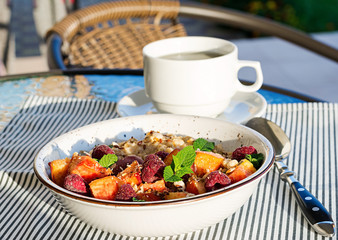 Oatmeal porridge with raspberry and peach on table. Healthy breakfast. Breakfast on the terrace