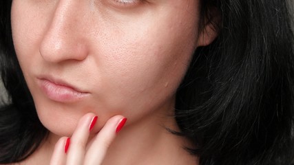 Female face close-up. Skin texture with enlarged pores. The girl touches the fingers of the problem...