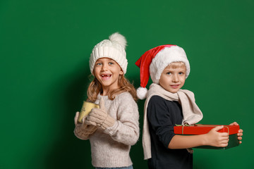 Cute little children with Christmas gift and cup of hot chocolate on color background