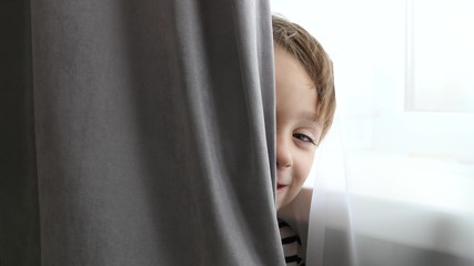 Happy kid playing hide and seek. The boy looks out and smiles.