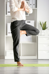 Fototapeta na wymiar Young businesswoman practicing yoga in office