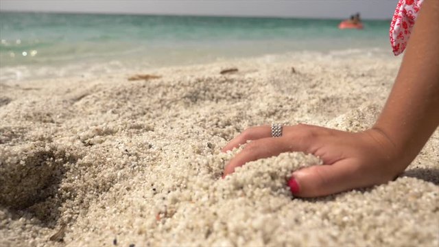 lady's hand touching white sand at the Mari Ermi beach in Sardinia Italy, In the background a stunning blue and green Mediterranean Sea.