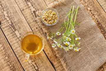 Glass cup of green tea with white chamomile flowers in a glass jar.