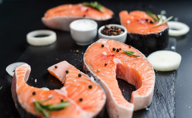 raw salmon steak on a dark stone background with onions, rosemary, spices, concept diet,...