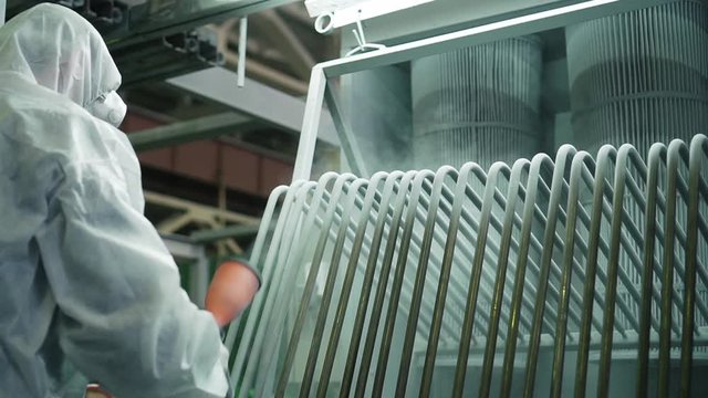 Worker in protective overalls works with hazardous chemicals, sprays it on metal