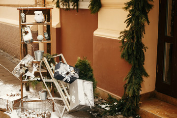  Stylish christmas gifts and rustic wooden sleigh with presents at front of store at holiday market in city street. Christmas street decor. Space for text. Rustic decoration