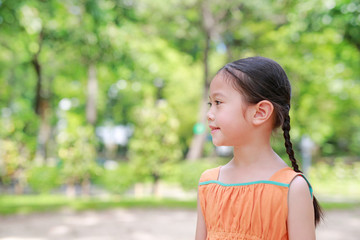 Fototapeta premium Smiling young little Asian child girl in the green garden. Close-up kid side view portrait.