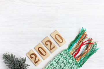 spruce branch, knitted scarf and number 2020 made up of wooden plates on the table Top view. background for warm wishes for the new year