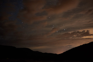 Night starry sky. Bright stars and constellations are visible through light clouds.