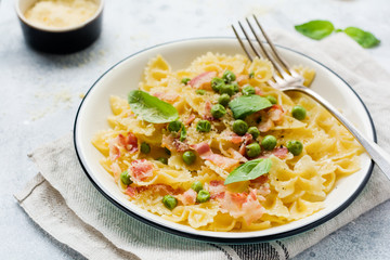 Fettuccine pasta with bacon and green peas and parmesan cheese in light plate on old gray concrete background. Top view.
