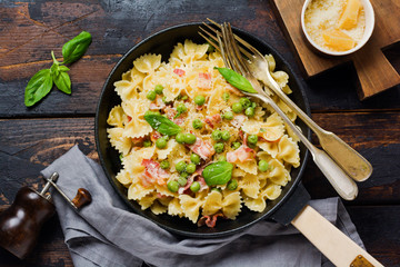 Fettuccine pasta with bacon and green peas and parmesan cheese in old pan on old dark wooden background. Top view.