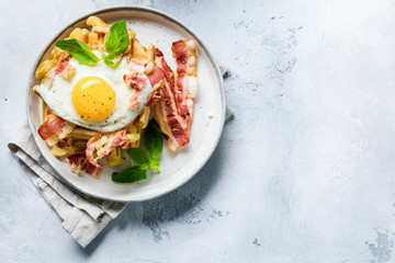 Cheese Waffles with fried bacon, egg and parmesan cheese with spices and basil for breakfast on light old concrete background. Top view.