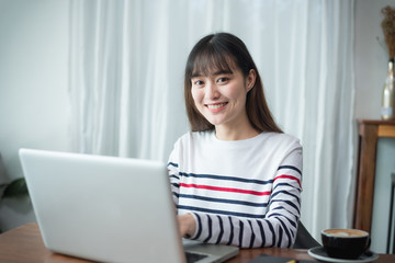 Young woman or student using laptop sitting at coffee shop. Happy girl working online or studying and using notebook. Freelance business concept.