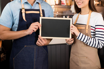 Young asian man and women barista holding blank chalkboard menu and smiling at coffee shop counter background, start up small business owner food and drink concept