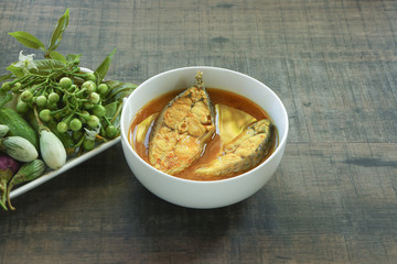 Yellow curry with fish in white bowl and vegetable on wooden background..