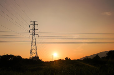 High voltage pole on sunset sky background ,  silhouette of tree and mountains  rural landscape view in the evening
