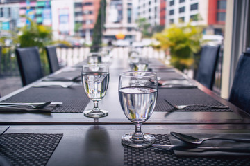 The tables and chairs in the restaurant with full set preparation next to the window with flare in the afternoon. 