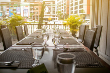 The tables and chairs in the restaurant with full set preparation next to the window with flare in the afternoon. 