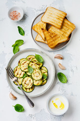 Grilled zucchini salad with basil leaves, yogurt sauce and fried bread in a simple ceramic plate on a white concrete background. Flat lay with copy space.