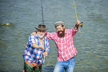 Male friendship. Father and son fishing. Summer weekend. Fishing together. Men stand in water. Nice catch concept. Fishing team. Happy fisherman with fishing rod and net. Hobby and sport activity