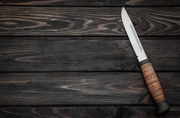 Hunting bowie knife with a wooden handle on dark wooden background. Steel arms weapon. top view