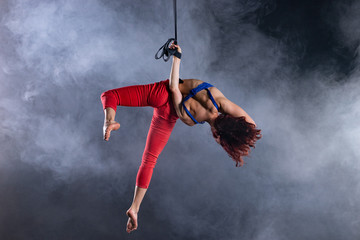 Fototapeta na wymiar Female athletic, sexy and flexible aerial circus artist with redhead on aerial straps on black background