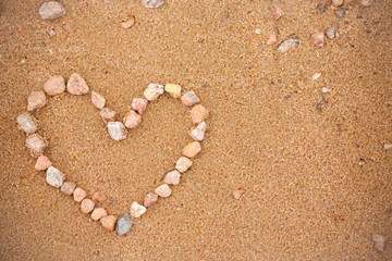 Fototapeta na wymiar Heart on the beach. A heart of small stones laid out on the sand. Photo background, concept with copyspace for wedding, valentines day and travel themes. Symbol of love on vacation.