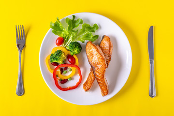Salmon steak grilled with vegetables on yellow paper background. Healthy food concept.