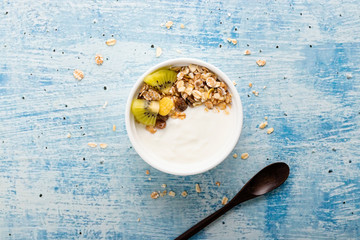 Top view of yogurt in bowl with granola,fresh kiwi  on wooden table. Health food concept.