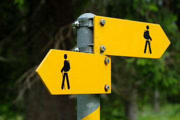 Yellow sign for swiss hiking trails on a metal mast points to the right and to the left