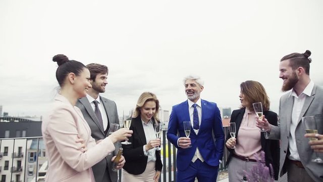 A group of joyful businesspeople having a party outdoors on roof terrace in city.
