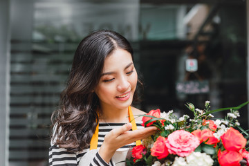 Smiling woman florist, small business flower shop owner, at counter, looking friendly at camera working at a special flower arrangement.