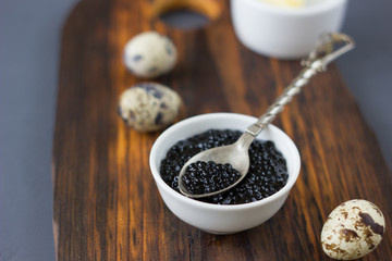 Black caviar with quail eggs over wooden board.