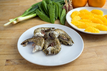 Raw black tiger prawn shrimps, orange slices and vegetables, cooking ingredients for a tasty dish on a wooden kitchen worktop