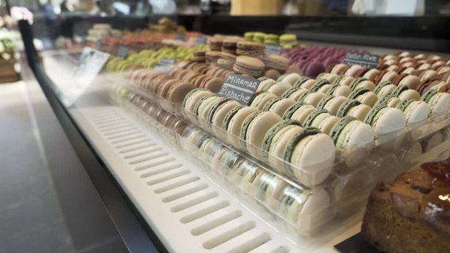 Assortment of colorful traditional French macarons laying in rows on market counter, food concept. Action. Colorful cakes on the counter of the store, sweet meringue-based confection, close up.