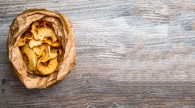 Tasty Apple Chips In Paper Bag On Wooden Table, Healthy Snack Of Apples Diet Dish. Space For Copy