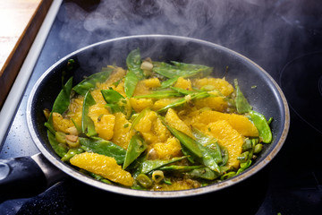 sugar peas, orange slices and spring onions roasted in a steaming pan, cooking healthy vegetarian food for a low carb vegetable meal