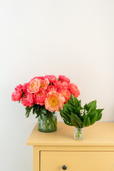 Coral peonies and spring lilies of the valley in a glass vase on wooden table.. Beautiful peony flower for catalog or online store. Floral shop concept . Beautiful fresh cut bouquet. Flowers delivery.