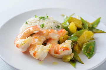 fried tiger prawn shrimps with vegetables from sugar peas and oranges, served with rice on a white plate, selected focus, narrow depth of field