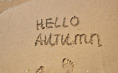 The words Hello autumn written on sand.